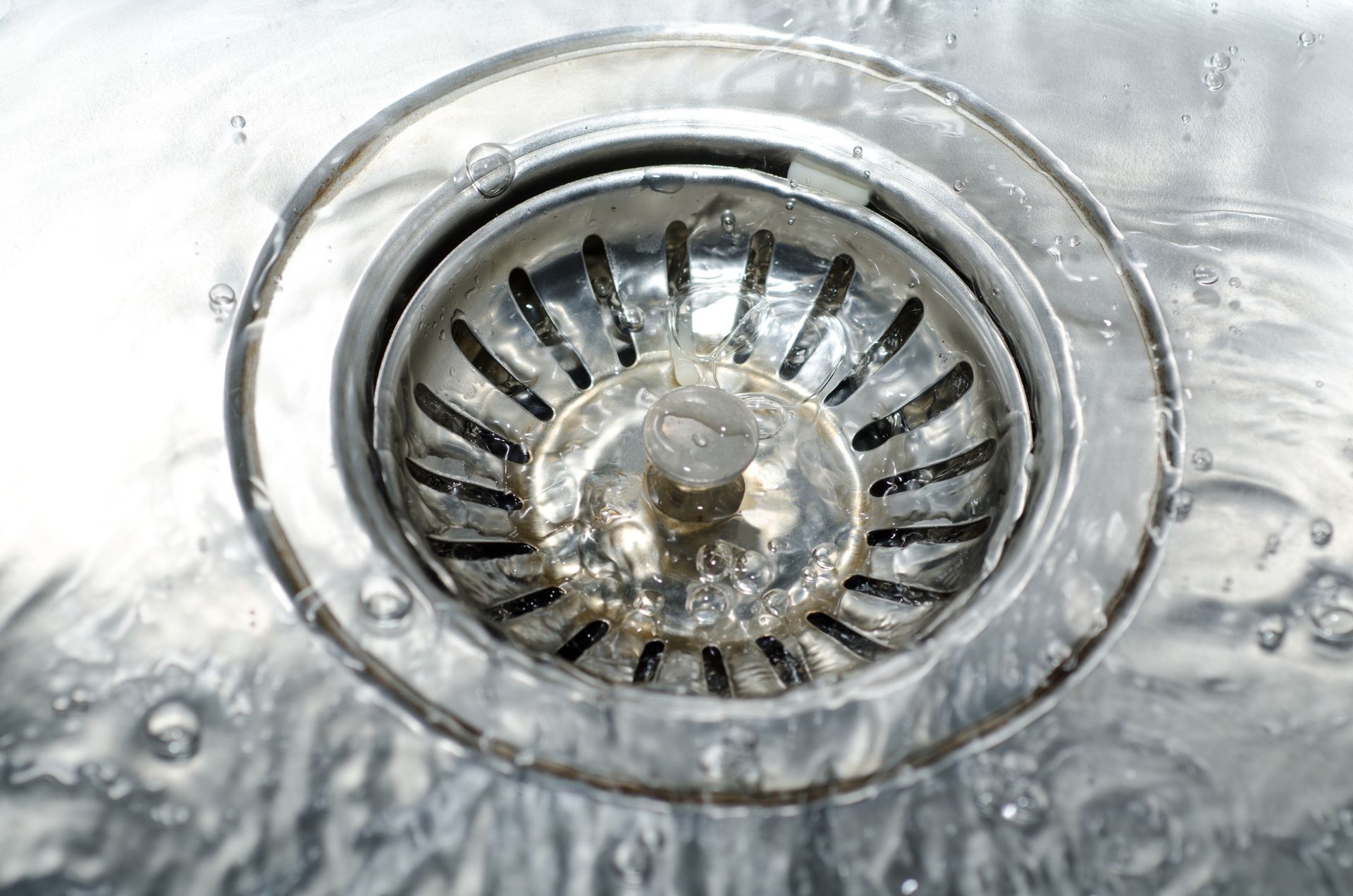 A stainless steel kitchen sink drain with water flowing through it.