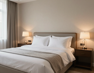 Neatly made bed with white linens and bedside lamps in a softly lit hotel room