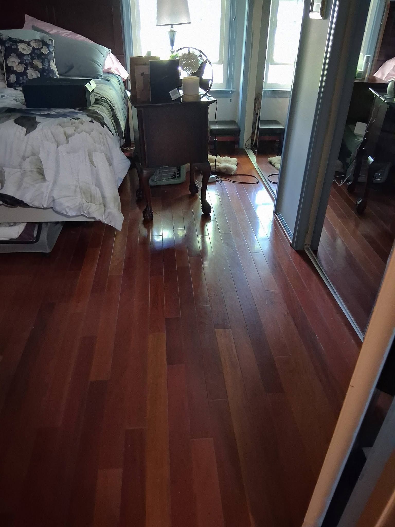 Bedroom with hardwood floor, bed on left, dresser by window, and mirrored closet doors on right.