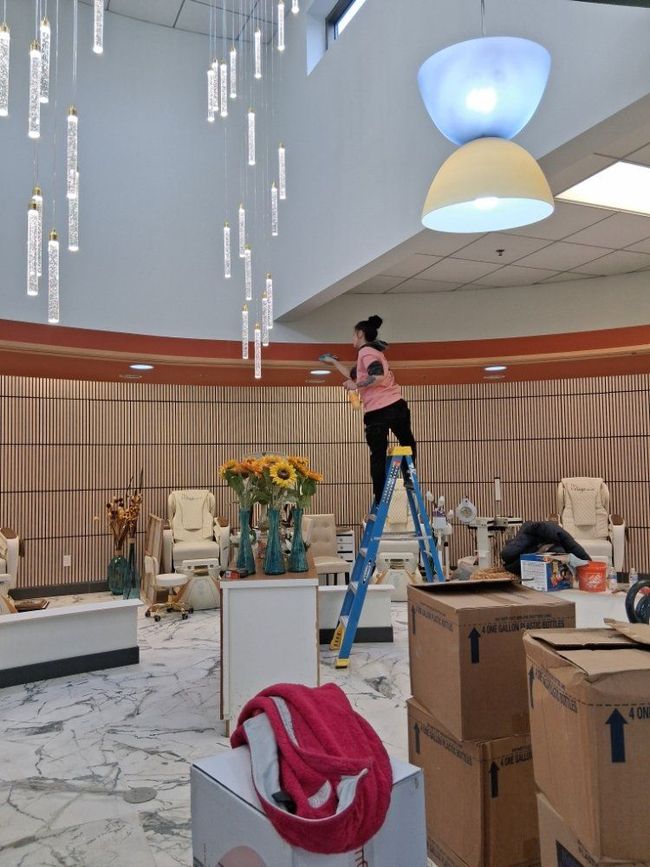 Worker on blue ladder installing ceiling lights in a hotel lobby under renovation.
