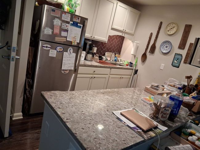 Kitchen with granite island, stainless fridge covered in notes, white cabinets, and dishes on the counter.