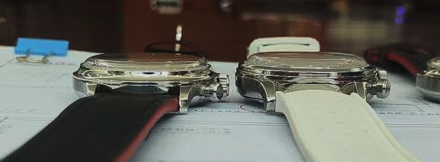 Two wristwatches with shiny metal cases and different colored silicone straps sit side-by-side on a white surface.