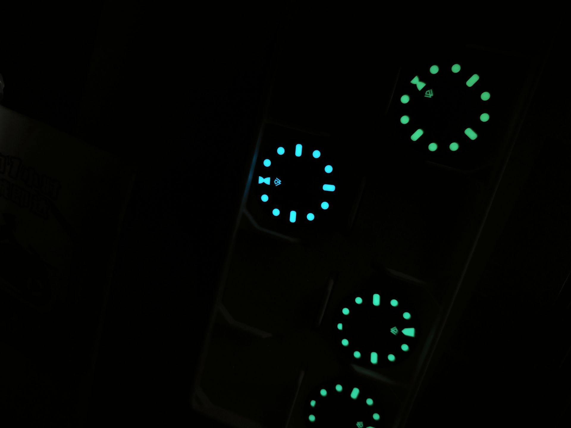 Glowing watch faces in various shades of blue and green against a dark background, showing the time.