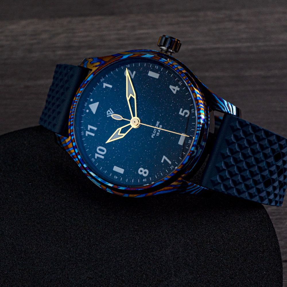 A dark blue starry dial watch with gold hands and a patterned, multi-colored bezel on a textured black rubber strap.