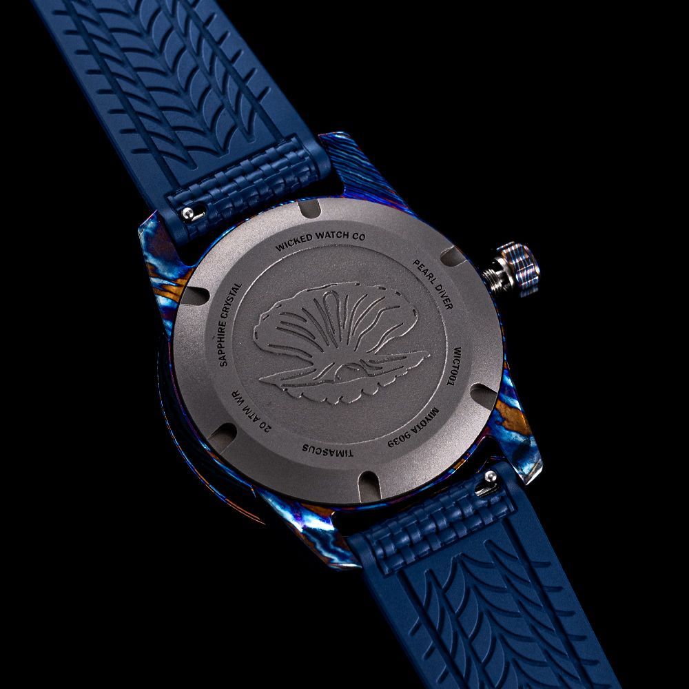 Close-up of the back of a watch case featuring an embossed seashell logo, with a dark blue patterned rubber strap.