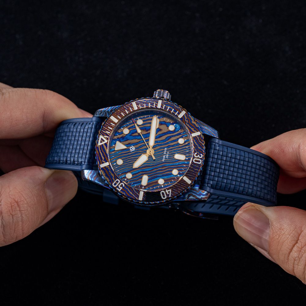 Close-up of hands holding a blue patterned dive watch with a textured rubber strap against a dark background.