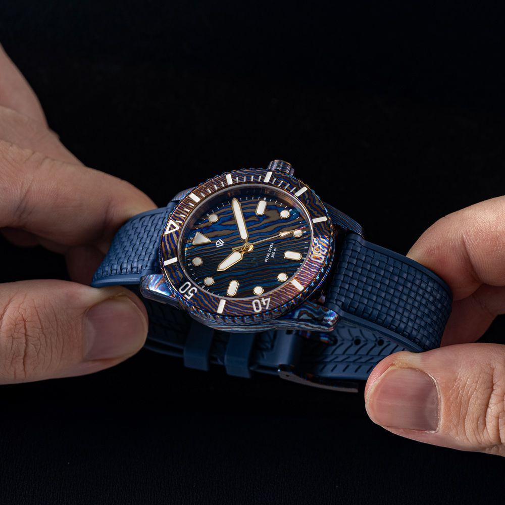 Close-up of hands holding a blue divers watch with a wavy dial pattern and a textured rubber strap against a black ground.