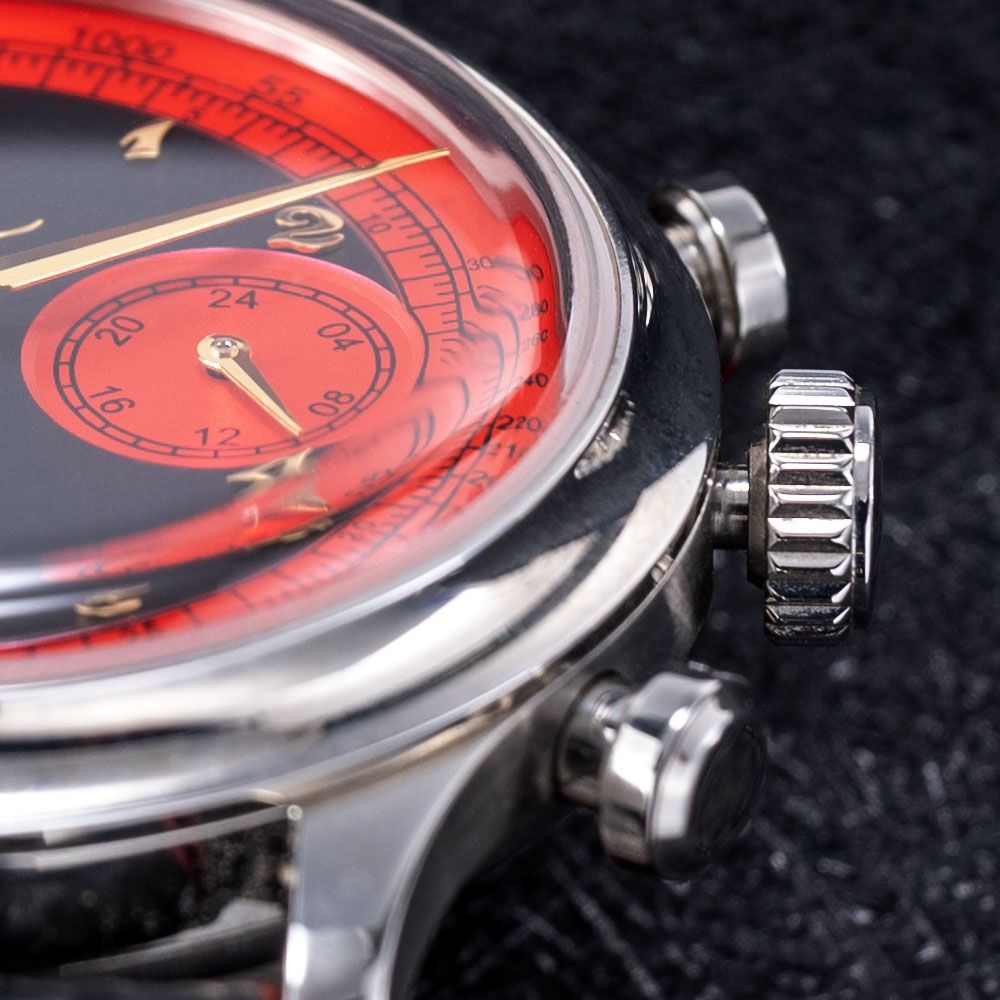 A close-up view of a silver wristwatch with a black face, red accents, and a domed crystal on a dark, textured surface.