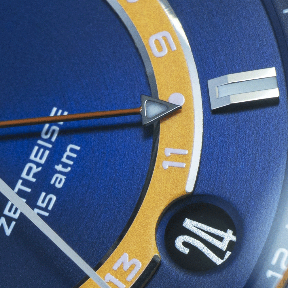 Close-up of a watch face with a blue background, gold-toned GMT ring, an arrow-tipped hand pointing to ten, and date 24.