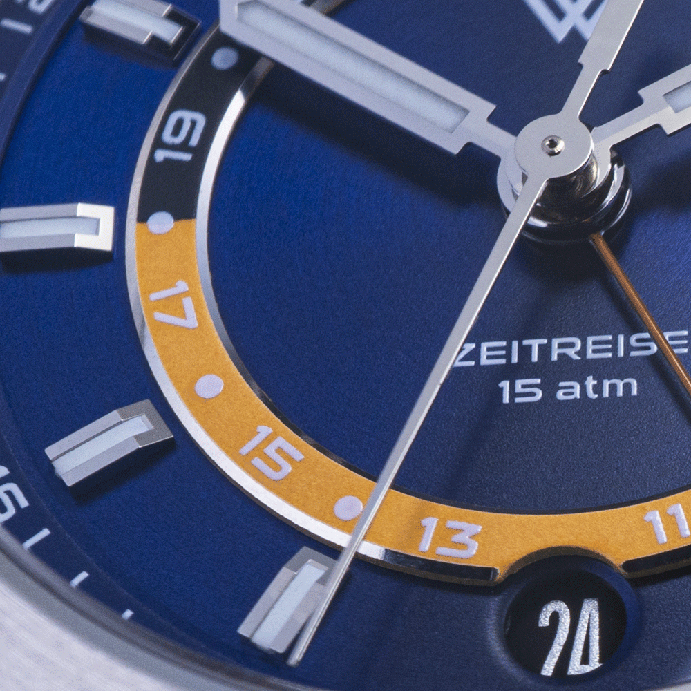 A close-up of a blue watch face with a yellow inner ring, white markings, silver hands, and a 