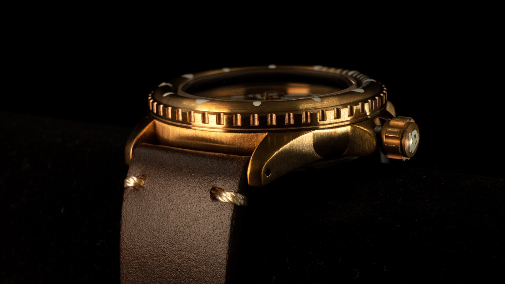 A close up of a gold watch with a brown leather strap on a black background.