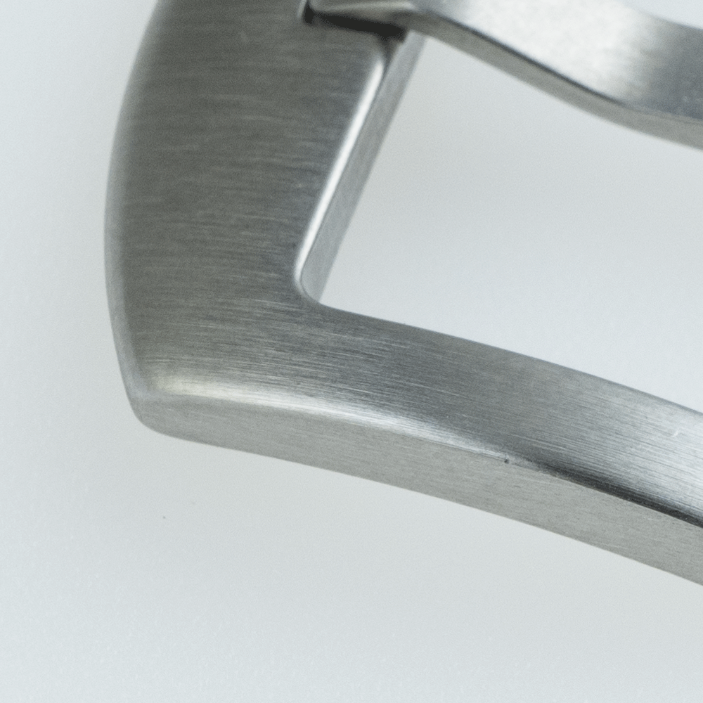 A close up of a stainless steel watch buckle on a white surface.