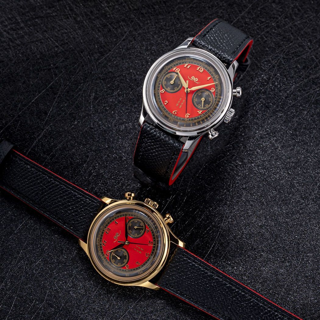 Two luxury chronograph watches with red faces and black textured straps against a black, grainy background.