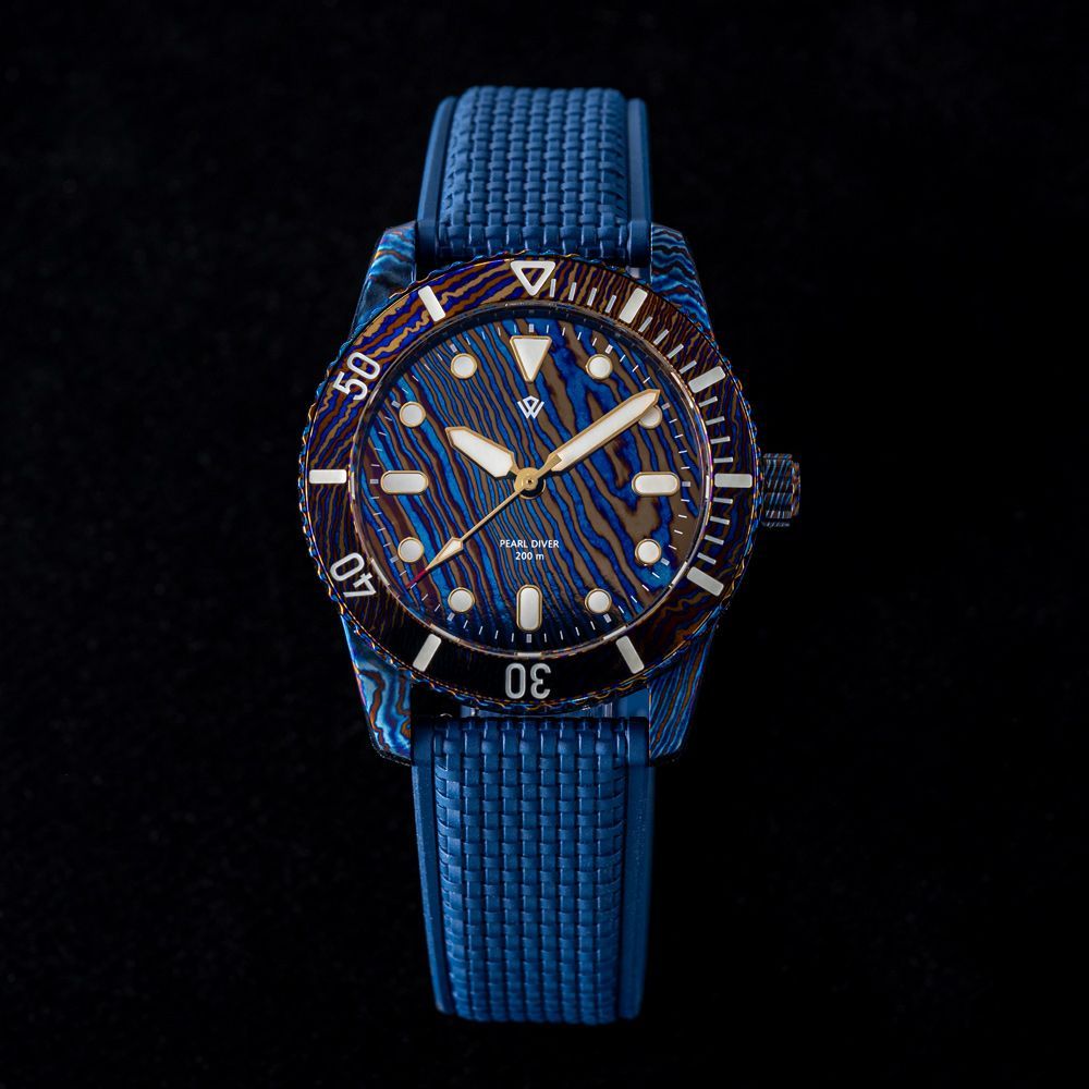 A dive watch with a wavy blue and bronze patterned dial and bezel, featuring a blue textured strap against a black background.