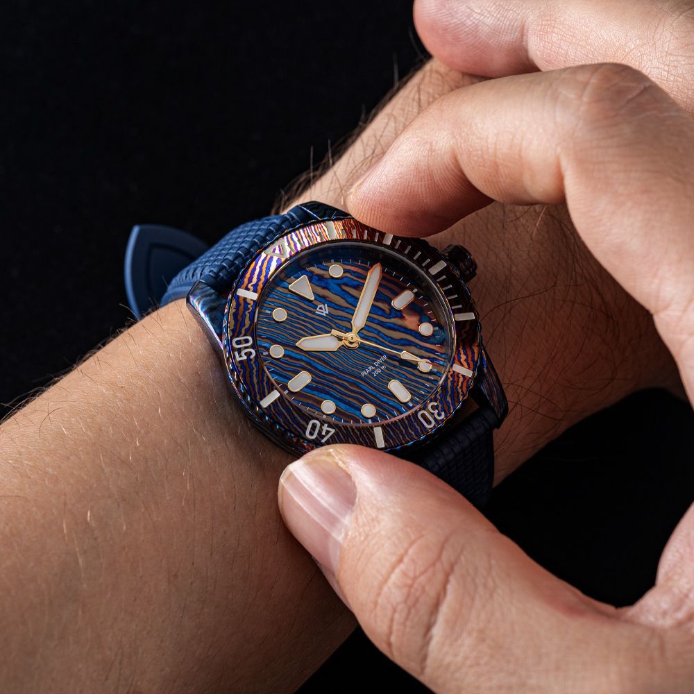 A person adjusting the bezel of a dark blue, patterned diver's watch with a matching blue strap.