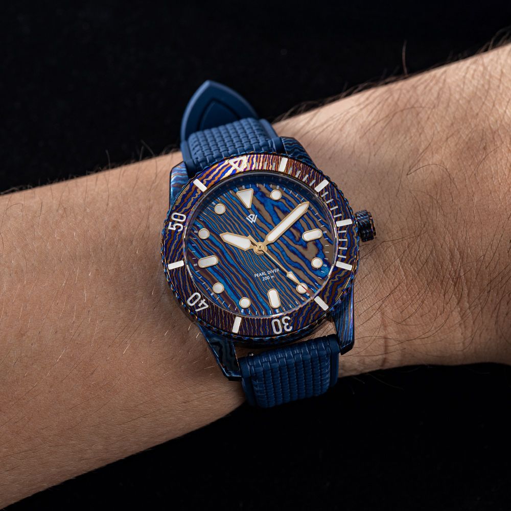 A wrist wearing a dive watch with a wavy blue patterned dial, a matching bezel, and a blue textured rubber strap.