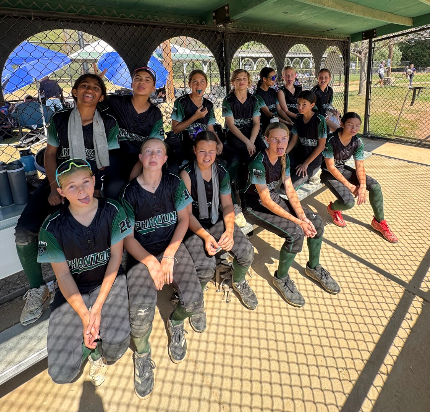 Group of people in matching dark uniforms sitting together under a shaded canopy, smiling at the camera.