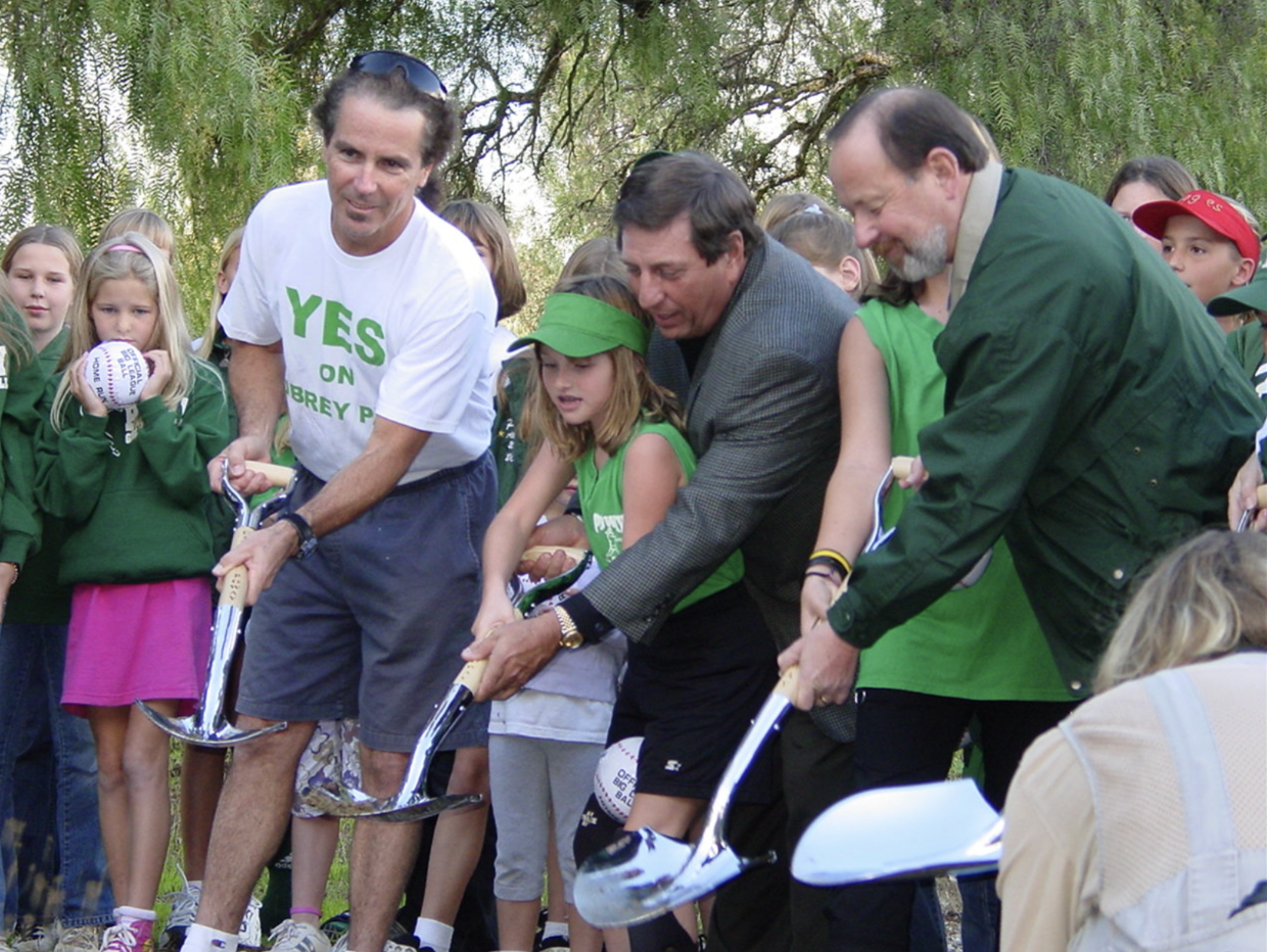 People pushing a child in a green helmet on a bike starting line outdoors