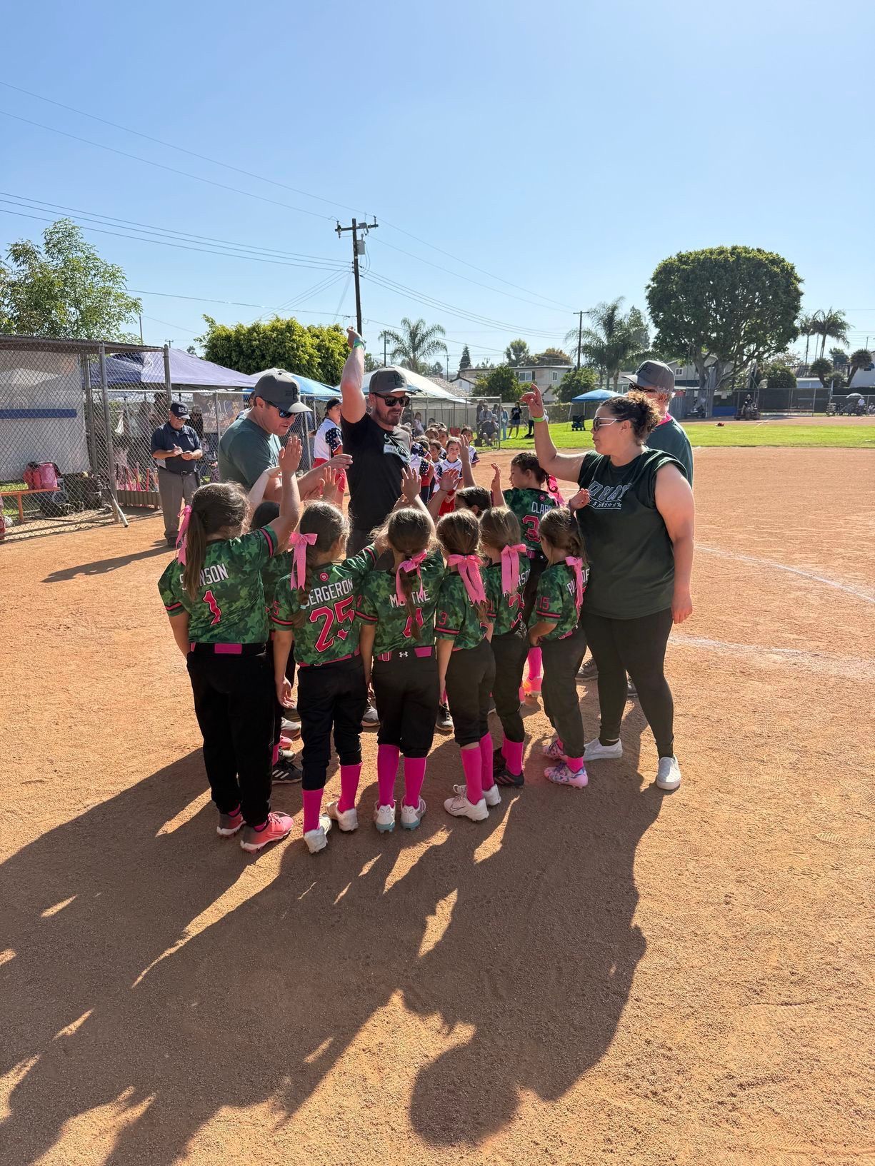 Softball players standing in a circle putting their hands together while standing on a dirt field