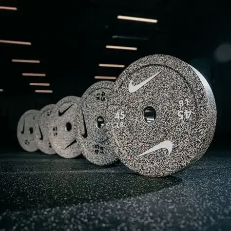 A rack of black, hexagonal dumbbells lined up in a gym with a brick wall background.