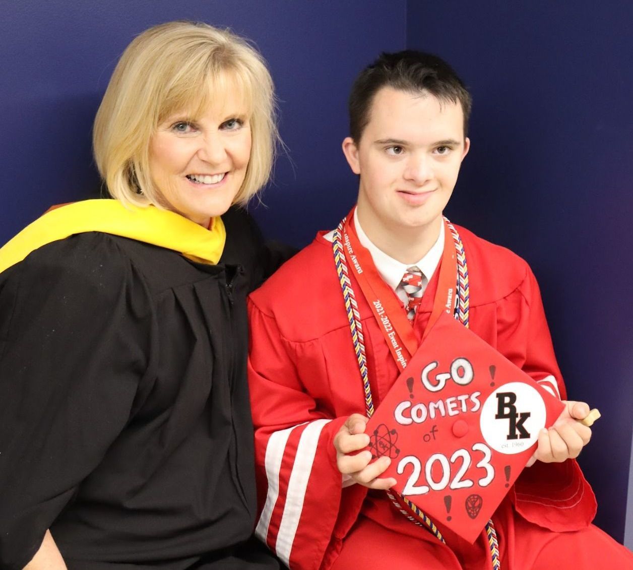 Woman in graduation attire poses with a smiling graduate holding a cap that says