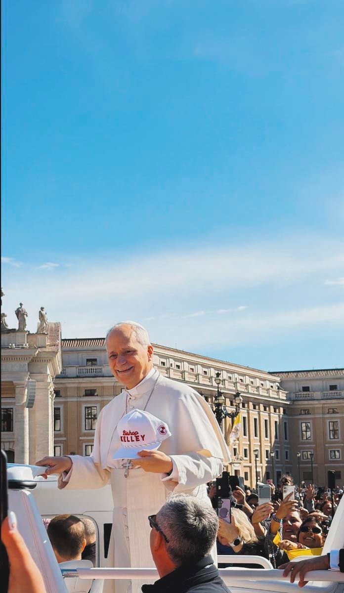 Pope Francis smiles and holds a cap with 