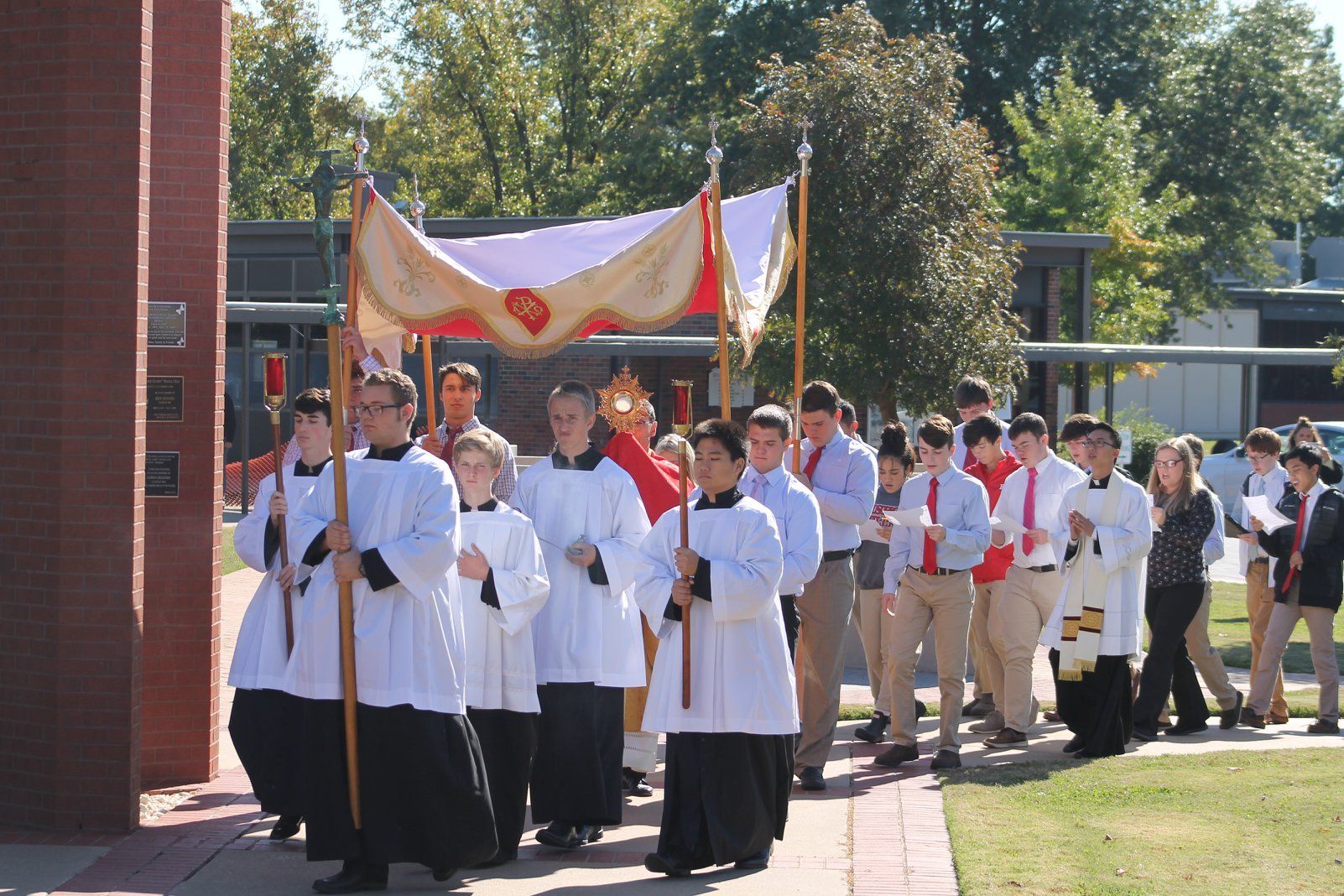 People in white robes and khaki pants processing outdoors under a banner at a formal ceremony
