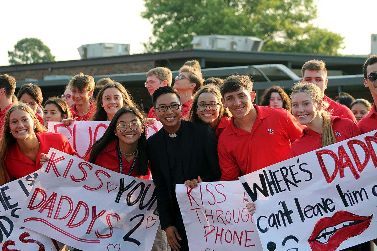Group of people in red shirts holding signs at a protest, smiling outdoors.