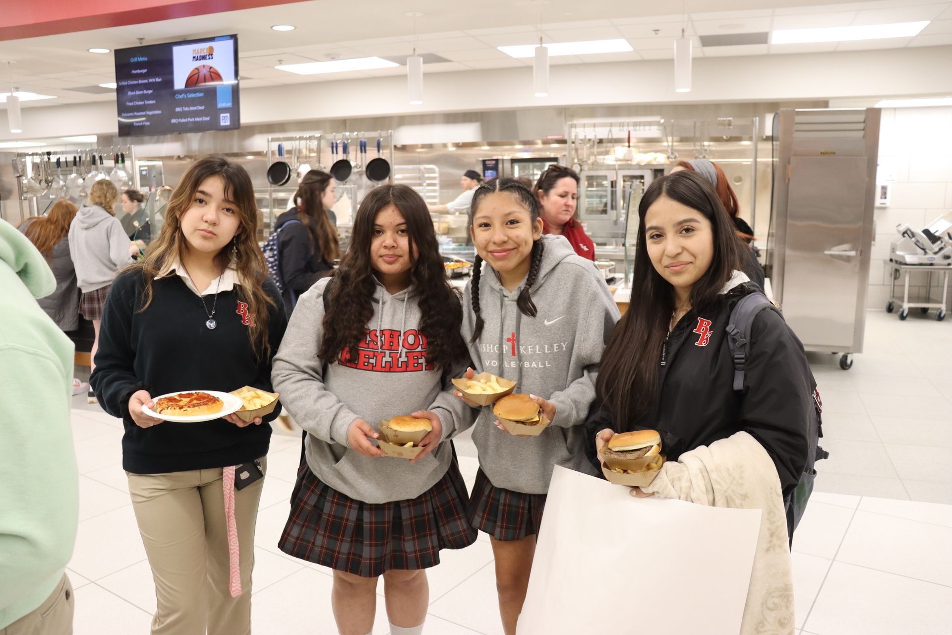 Four students in a school dining hall holding food.