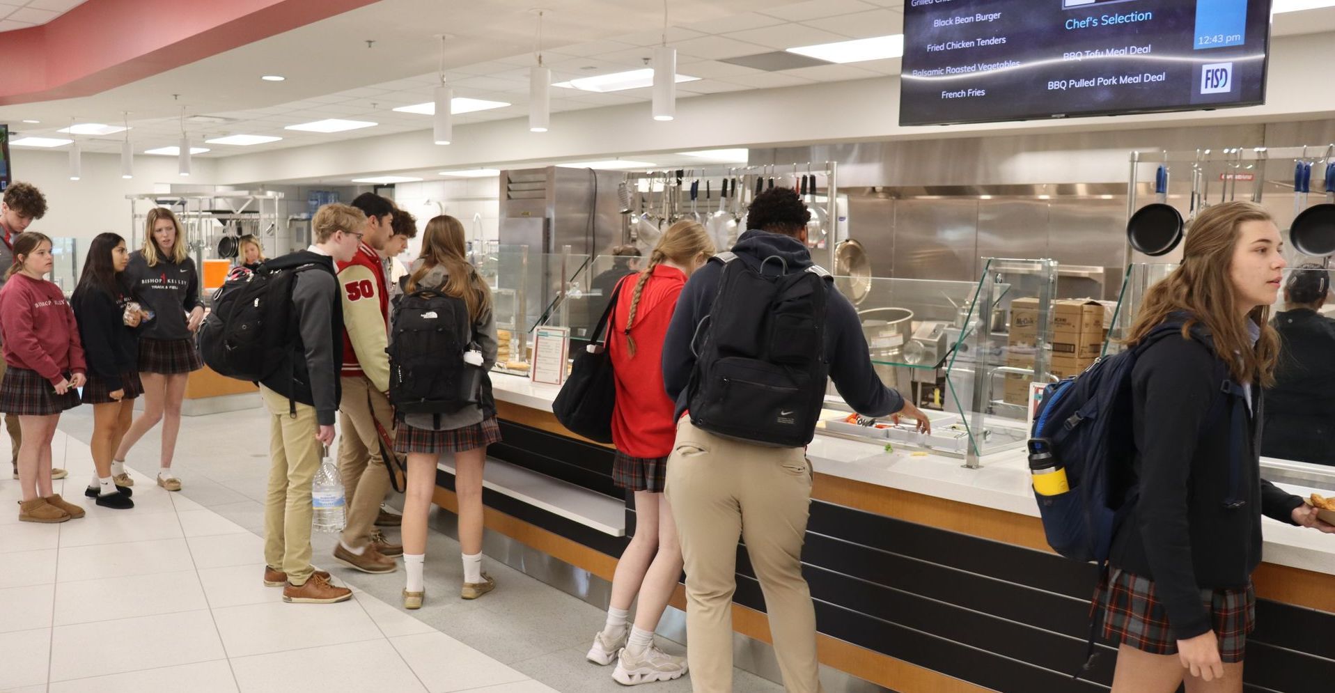 Students line up at a school dining hall food counter.