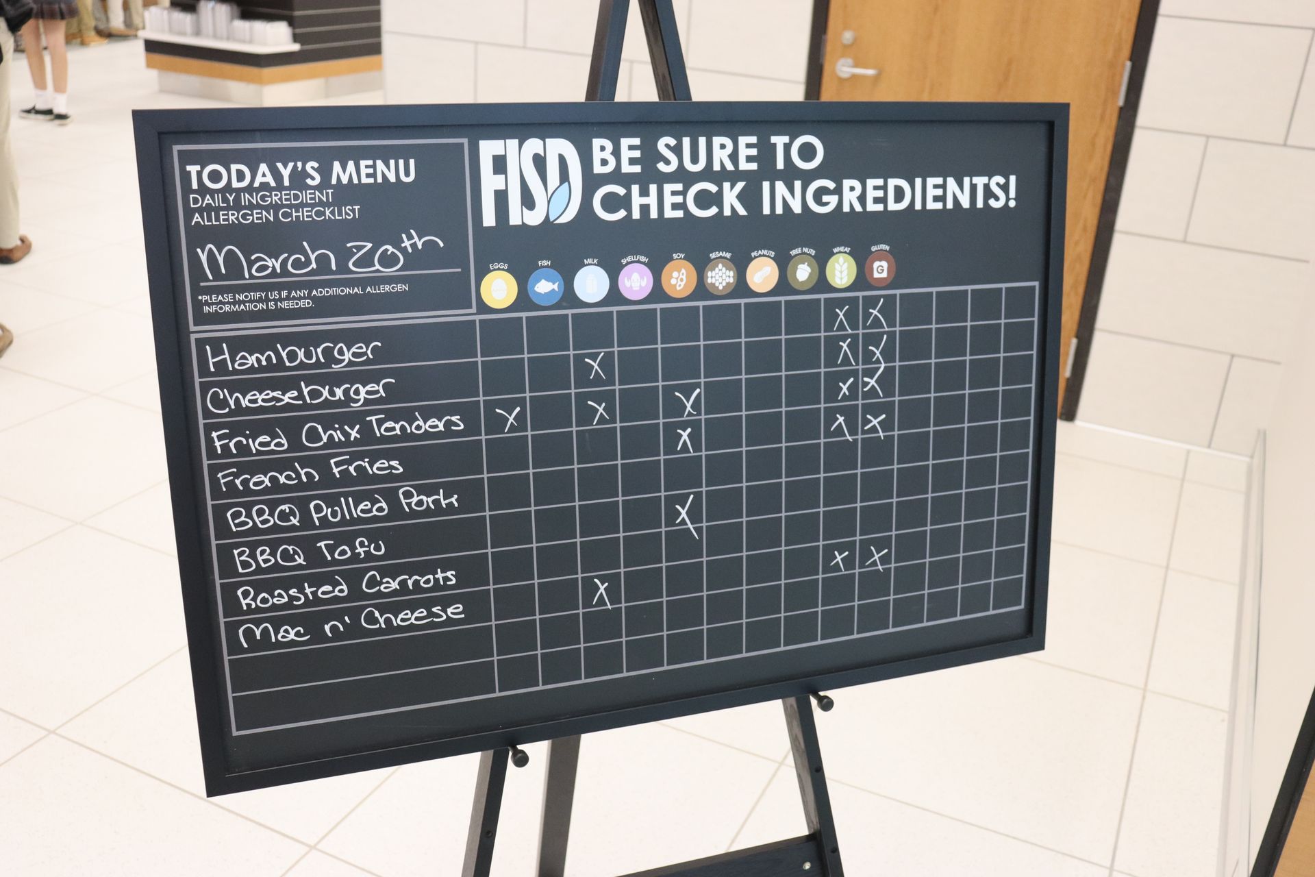 Menu board listing school lunch options for March 20th, with ingredient checkmarks.