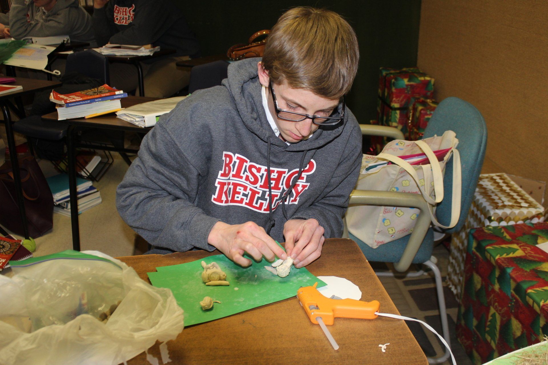 Person in a gray hoodie concentrating on a craft project at a table with green paper and tools