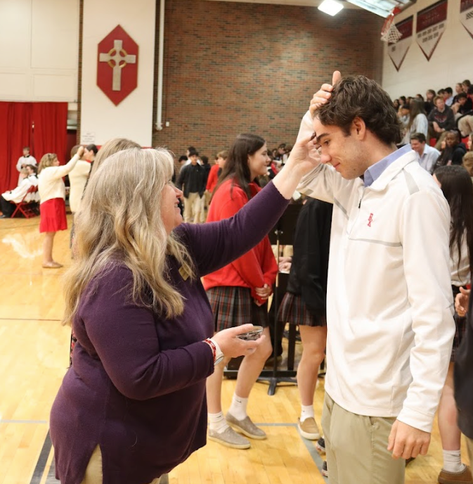 Woman with hand on man's forehead in a gymnasium. People in background.