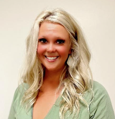 Blonde woman with long wavy hair, smiling, wearing a sage green shirt.