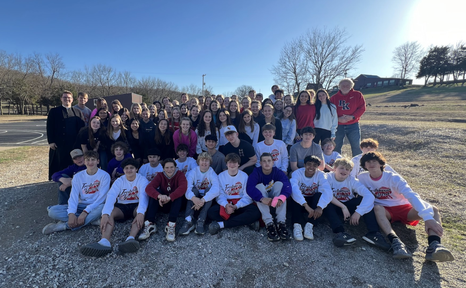 Large group of students in a field posing for a photo on a sunny day. Some wear matching shirts.