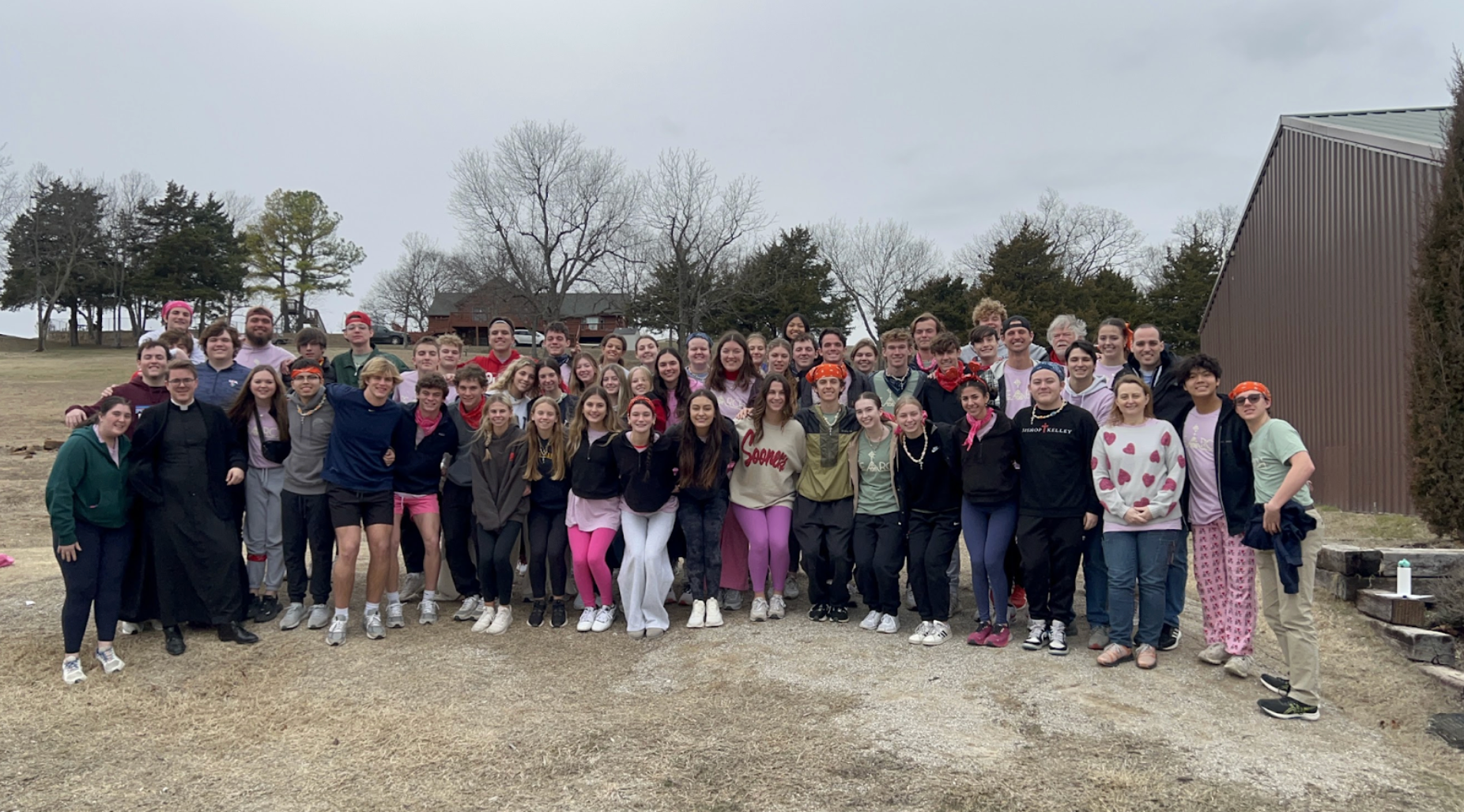Group of students posing outdoors; overcast sky. Many wearing casual clothes, smiling.