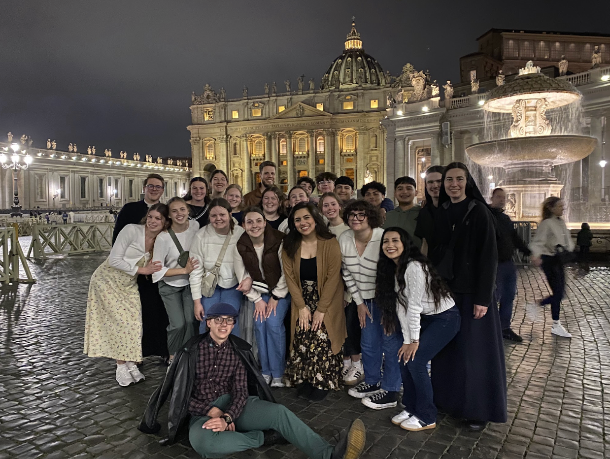 Group of students posing for a photo in front of St. Peter's Basilica at night.