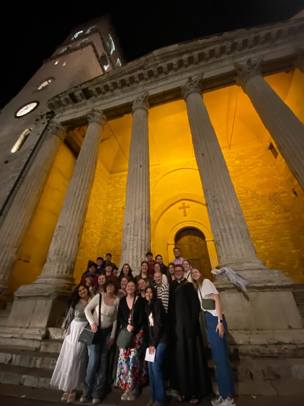 Group of people posing in front of a tall, illuminated building with columns at night.