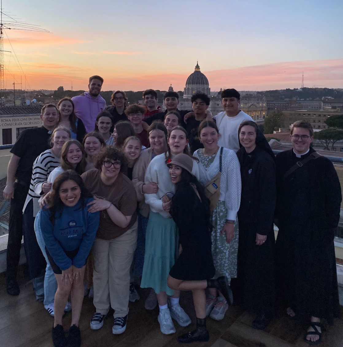 Group of students on a rooftop with a cityscape in the background; sunset colors.