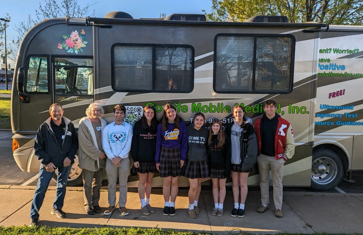 Group of students posing by a mobile unit with graphics, under blue sky.