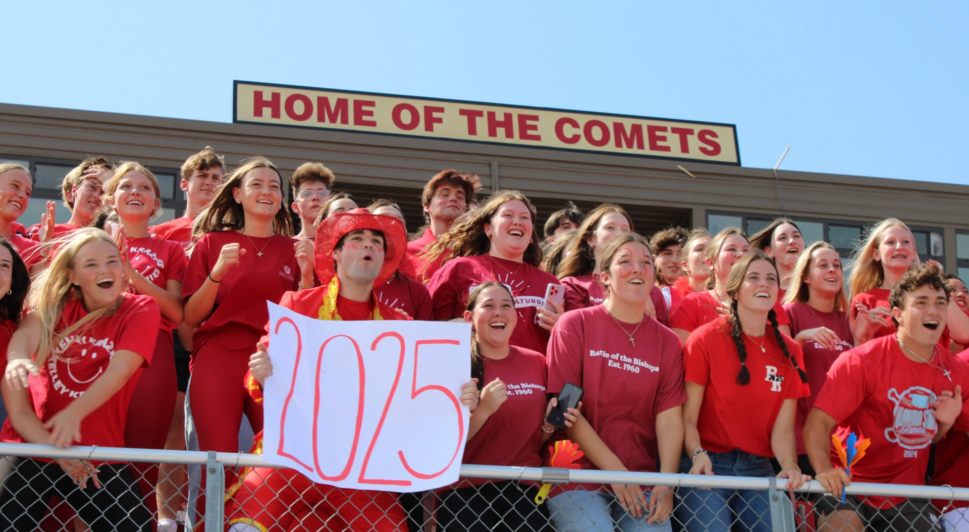 A crowd in red shirts cheering, holding a sign that says