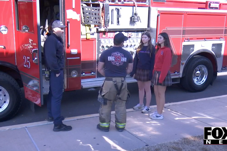 Two firefighters and two students stand by a red fire truck; Fox News logo.