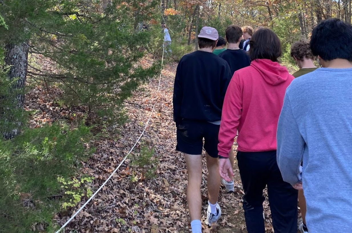A group of students hiking on a wooded trail. They are following a white rope.