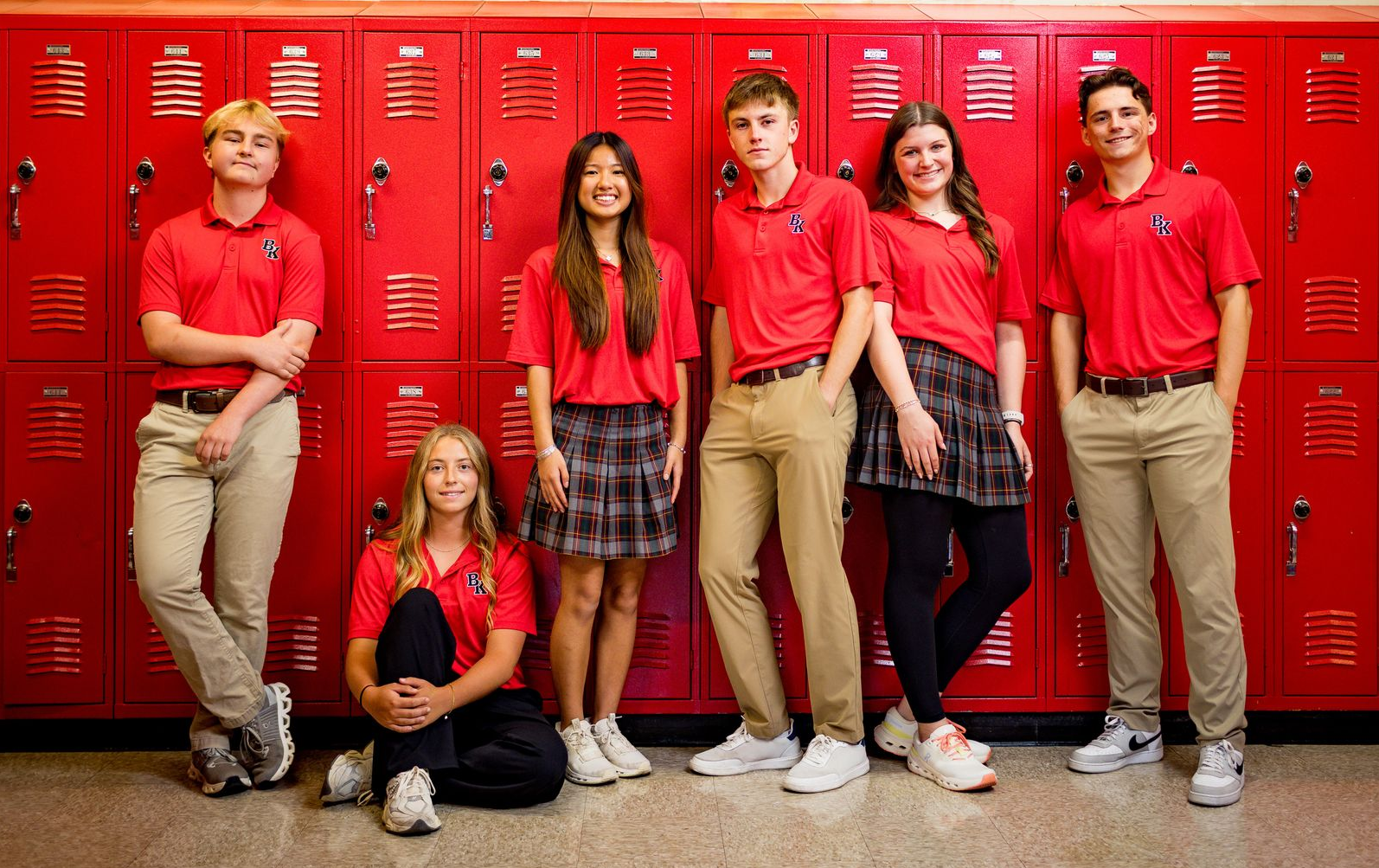 Six students in uniforms pose in front of red lockers for recognition photo.