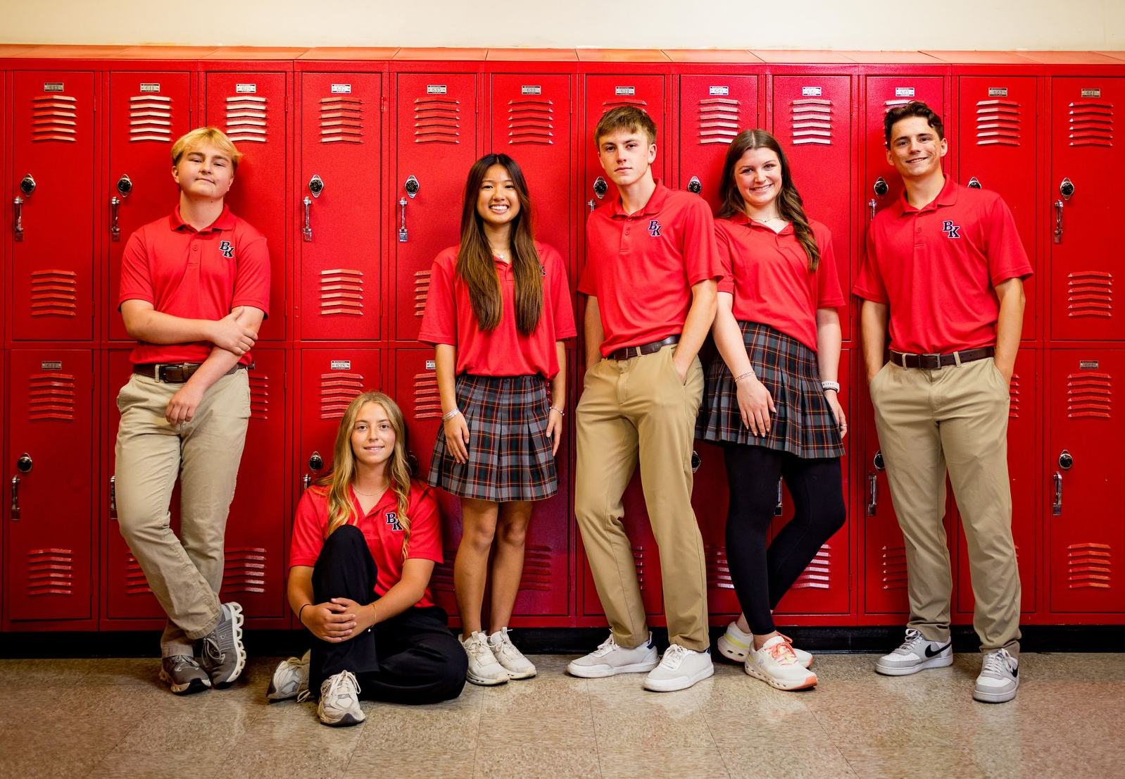 Six students in red shirts posing in front of red school lockers.
