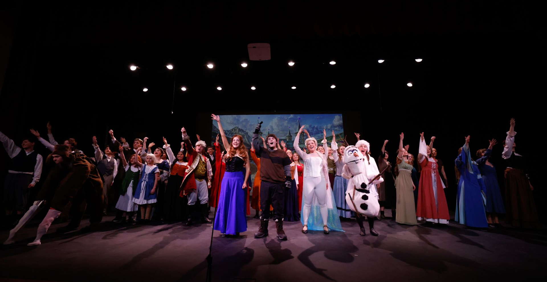 Group of performers on a stage, dancing in colorful costumes under bright spotlights