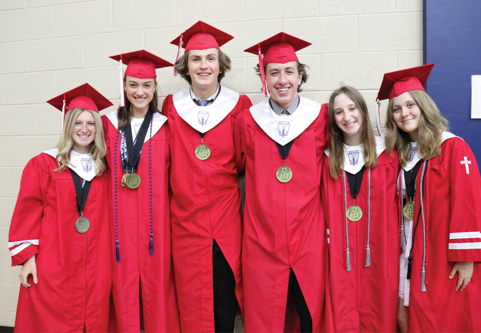 Graduates in red gowns and caps pose, each wearing a medal.