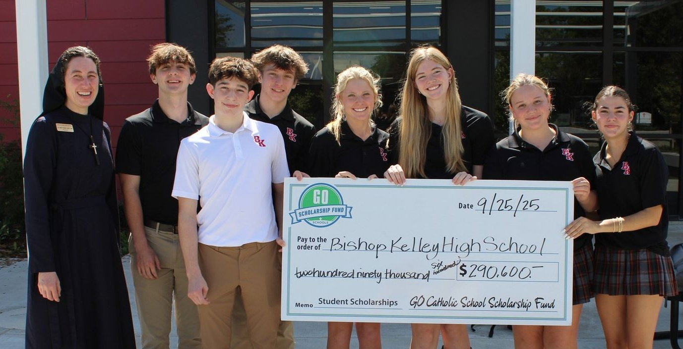 Group of students with Religious Sister of Mercy in habit holding a large check outside a building. Check recipients smile.