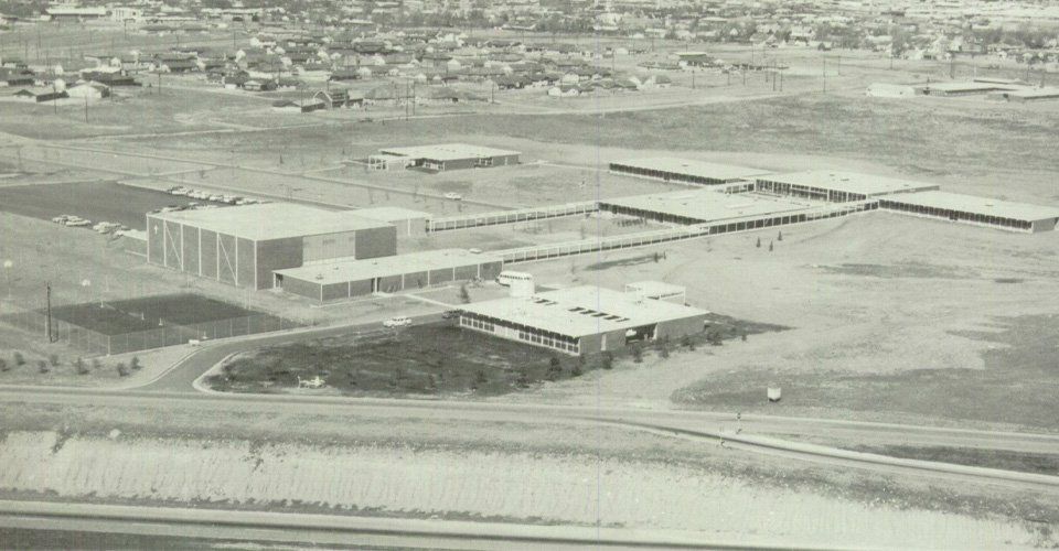 Aerial view of a large industrial building and open lot in a snowy landscape.