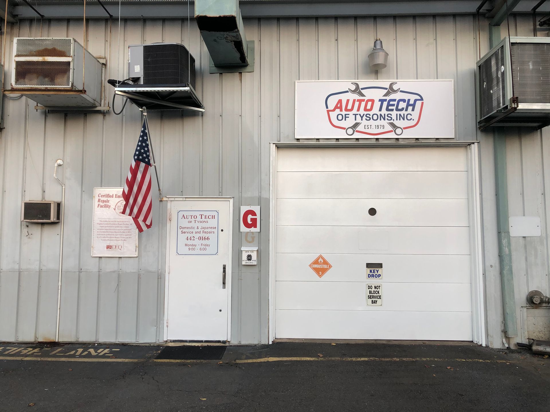 Exterior of Auto Tech of Tyrannus, a white building with garage door and American flag | Auto Tech of Tysons